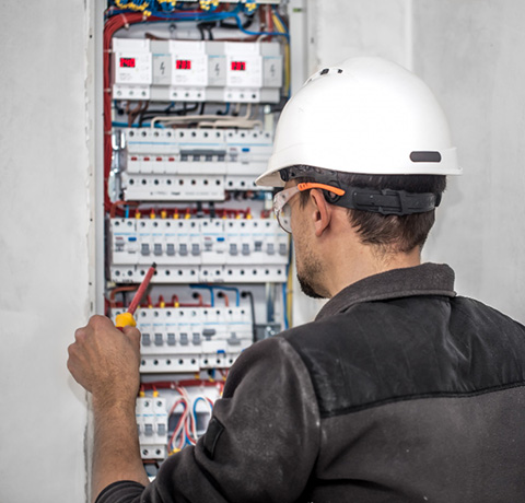 Photo d'un électricien réalisant les branchements et des vérifications sur un tableau électrique.