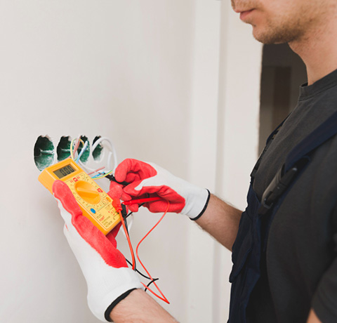 Photo d'un électricien qui teste une prise à l'aide d'un multimètre.